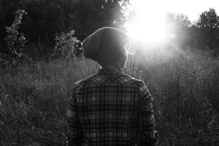 Nuori katsoo aurinkoa kohti niityllä, mustavalkoinen kuva.