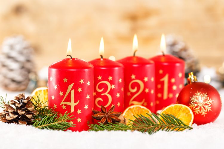 Neljä punaista adventtikynttilää palavat joulukoristeiden keskellä. Kynttilöissä on numerot 1,2,3 ja 4.