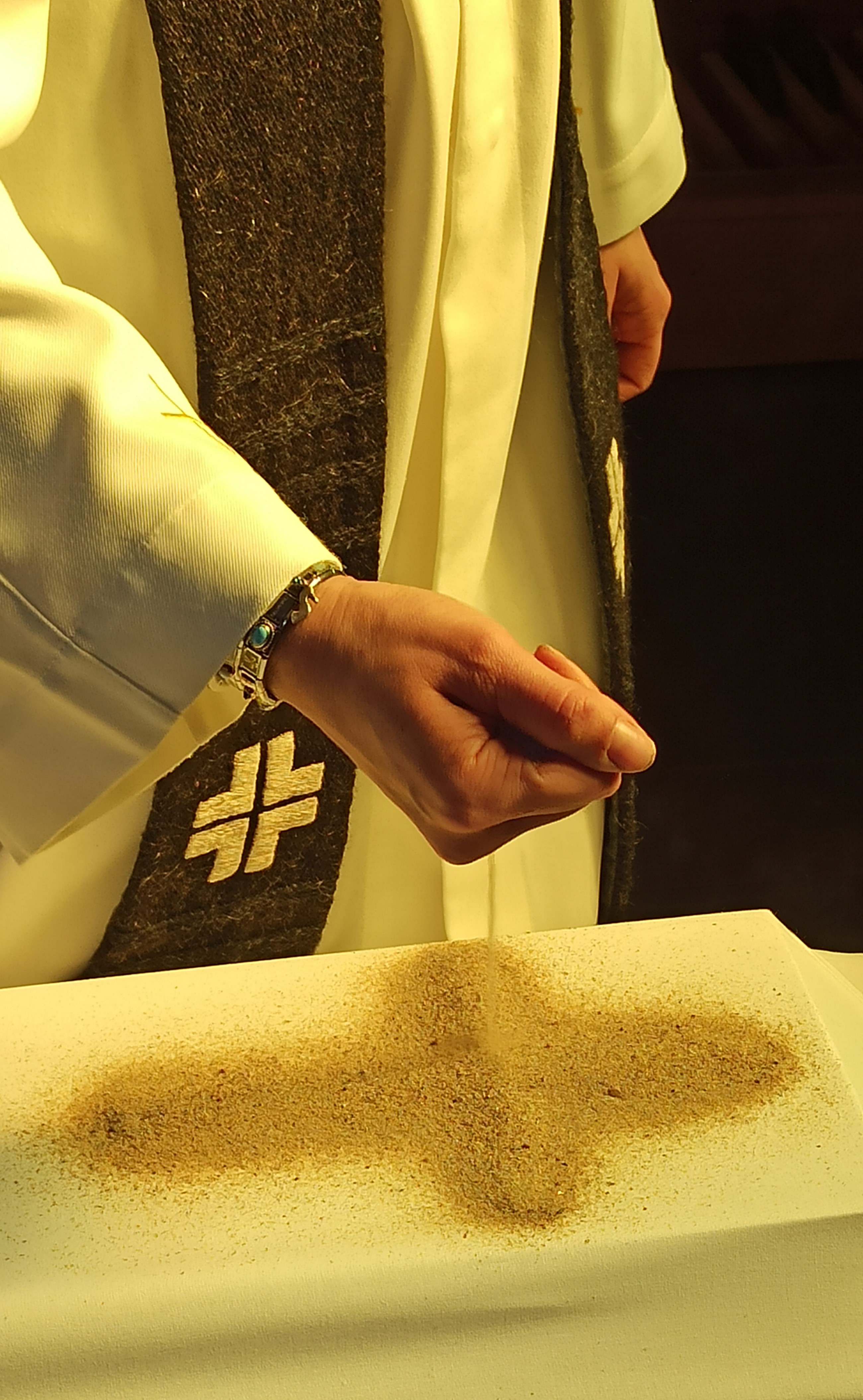 Pappi tekee hiekasta ristin arkun päälle.