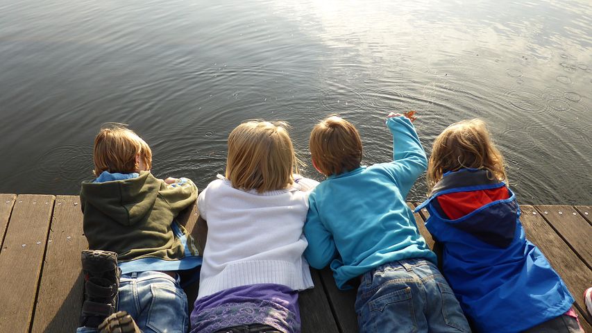 Neljä lasta makaavat laiturilla järven rannalla.
