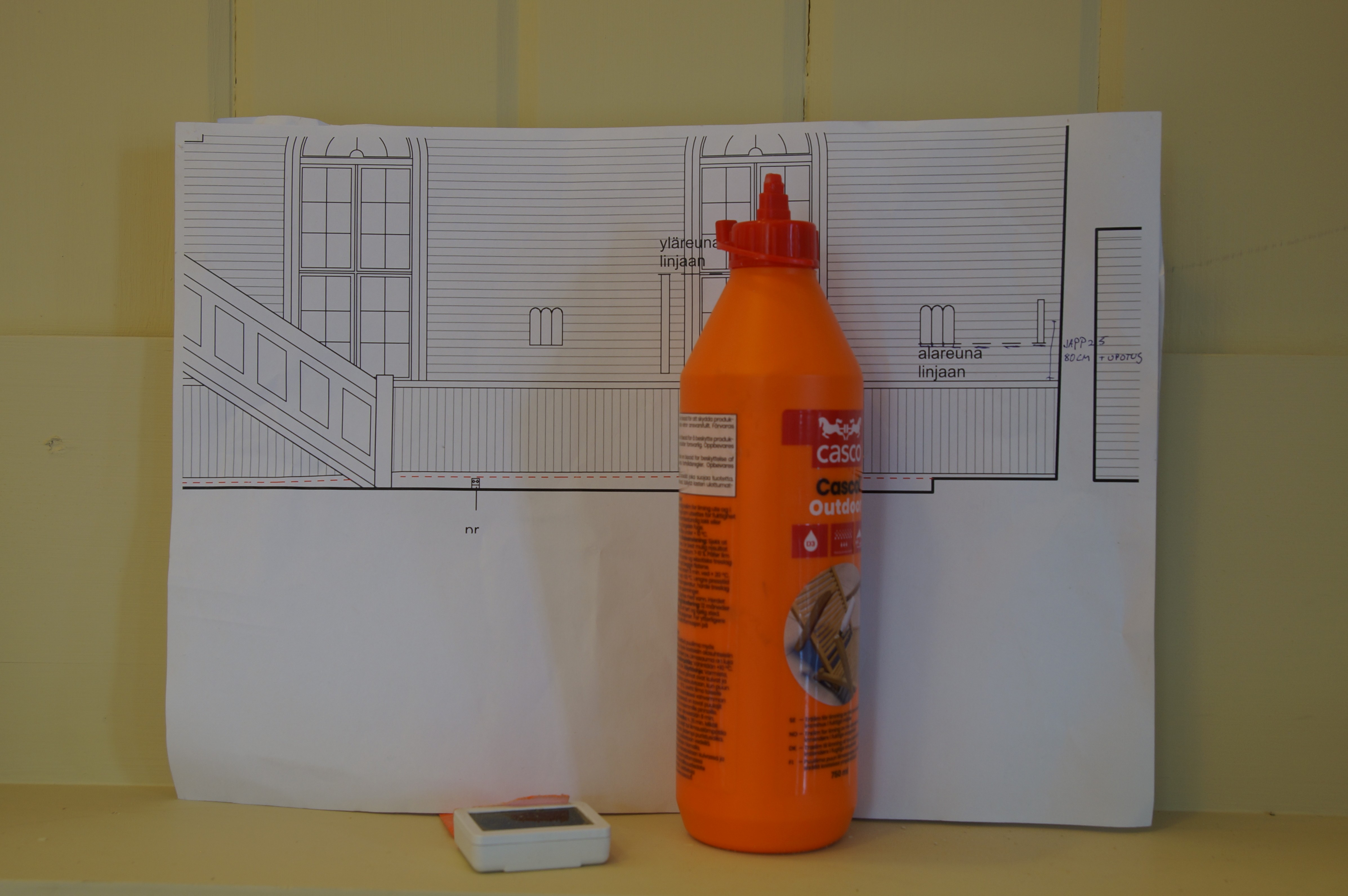 Virsikirjahylly, jonka päällä on piirros kirkosta sekä oranssi muovipullo.