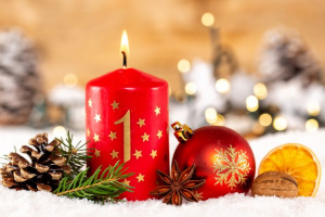 Ensimmäinen adventtikynttilä palaa joulukoristeiden keskellä. Kynttilässä on numero 1 ja se on punainen.