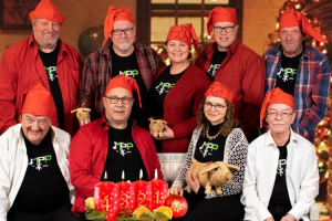 Laulu- ja soitinyhtye Mamma, Pappi ja Papat tonttulakit päässä. Heidän edessään palaa neljä adventtikynttilää. Kynttilöissä on numerot 1, 2, 3 ja 4 ja ne ovat punaisia.