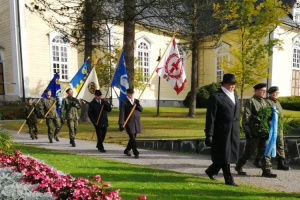 Lippukulkue ja seppelpartio kulkemassa kirkon edessä.