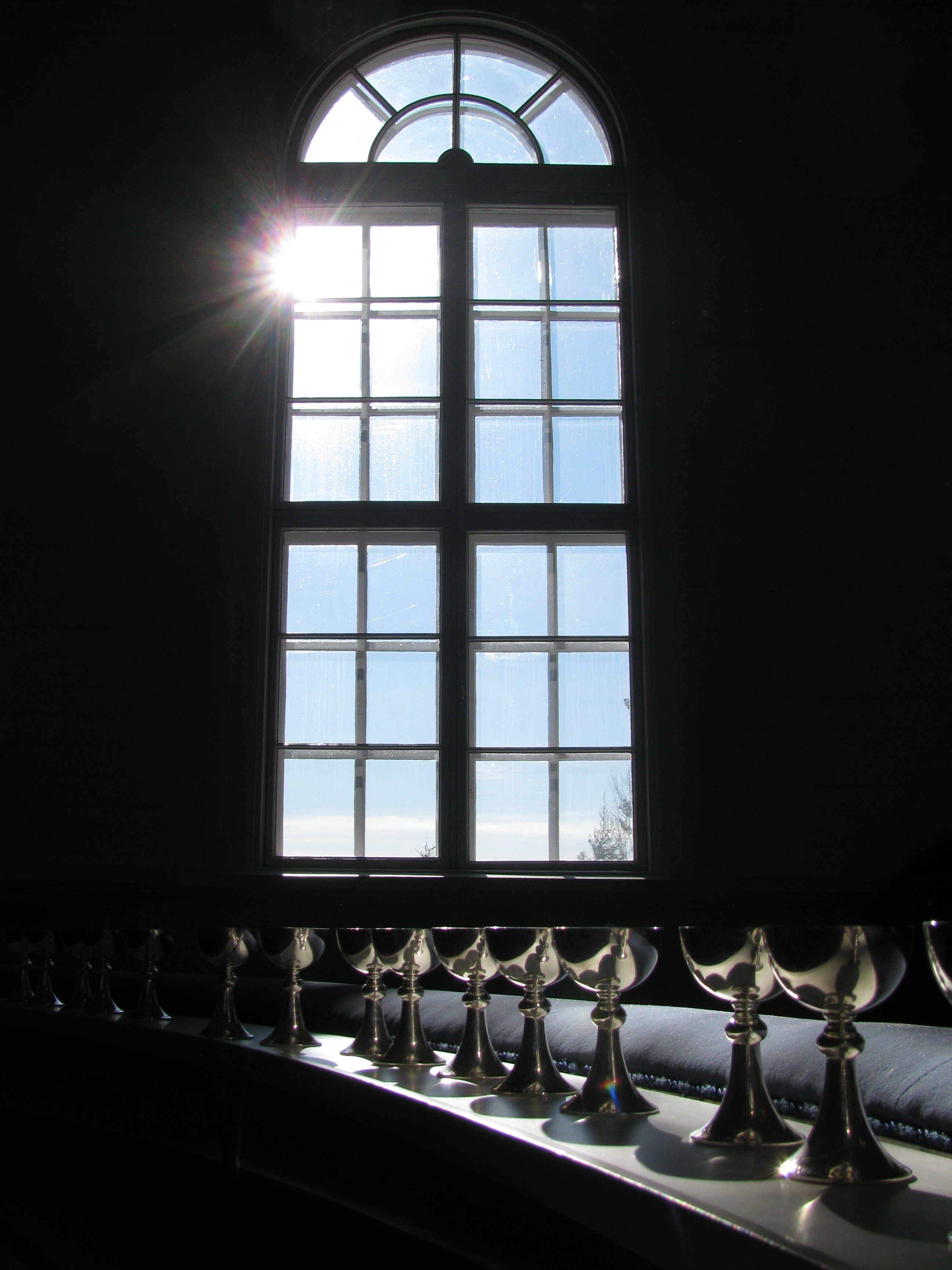 Kuvassa ehtoollispikareita alttarikaiteella. Pikareihin osuu auringonvalo ikkunasta.