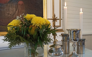 Hämeenkyrön kirkon alttarilla keltainen kukkakimppu, krusifiksi, kaksi kynttilää, ehtoollismalja ja leipärasia.