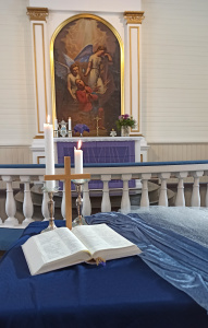 Hämeenkyrön kirkon alttari violetissa paastovärissä, etualalla Raamattu, risti ja kaksi kynttilää
