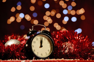 Kello, jonka näyttää keskiyötä sekä punaisia joulukuusen nauhoja ympärillä.