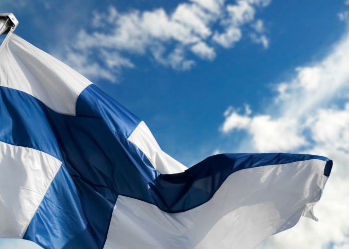 Suomen lippu ja sininen taivas, jossa valkoisia pilvenhattaroita.