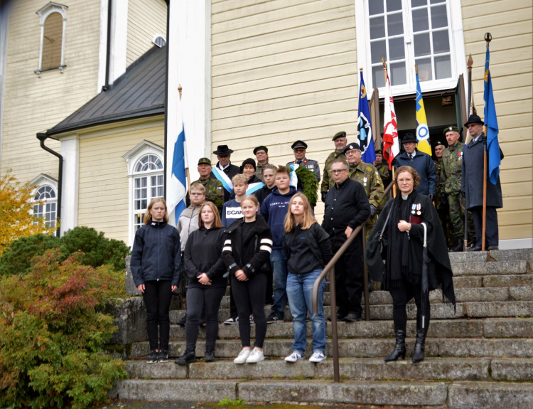 Lipun- ja seppeleenkantajat sekä muu maanpuolustusväki ennen seppeleenlaskua yhteiskuvassa kirkon portailla.