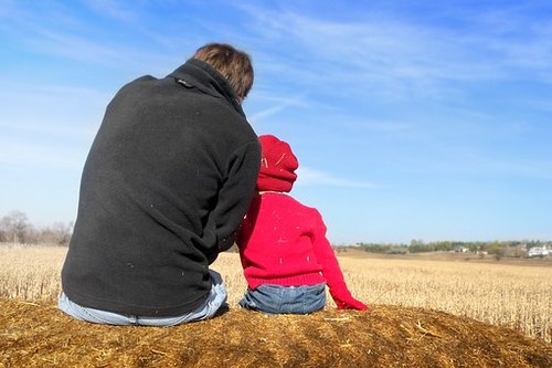 Vanhempi ja lapsi istuvat pellolla vierekkäin