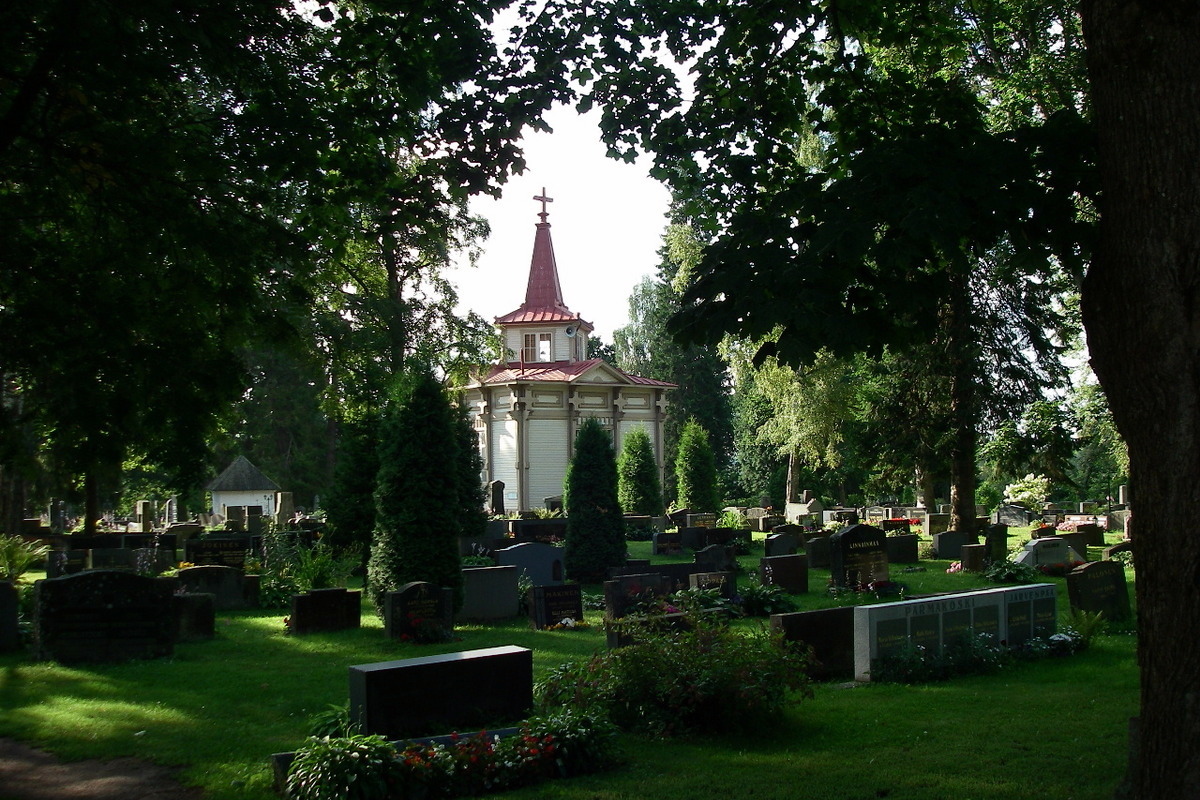 Vanha kappeli kesäisen vanhan hautausmaan keskellä.