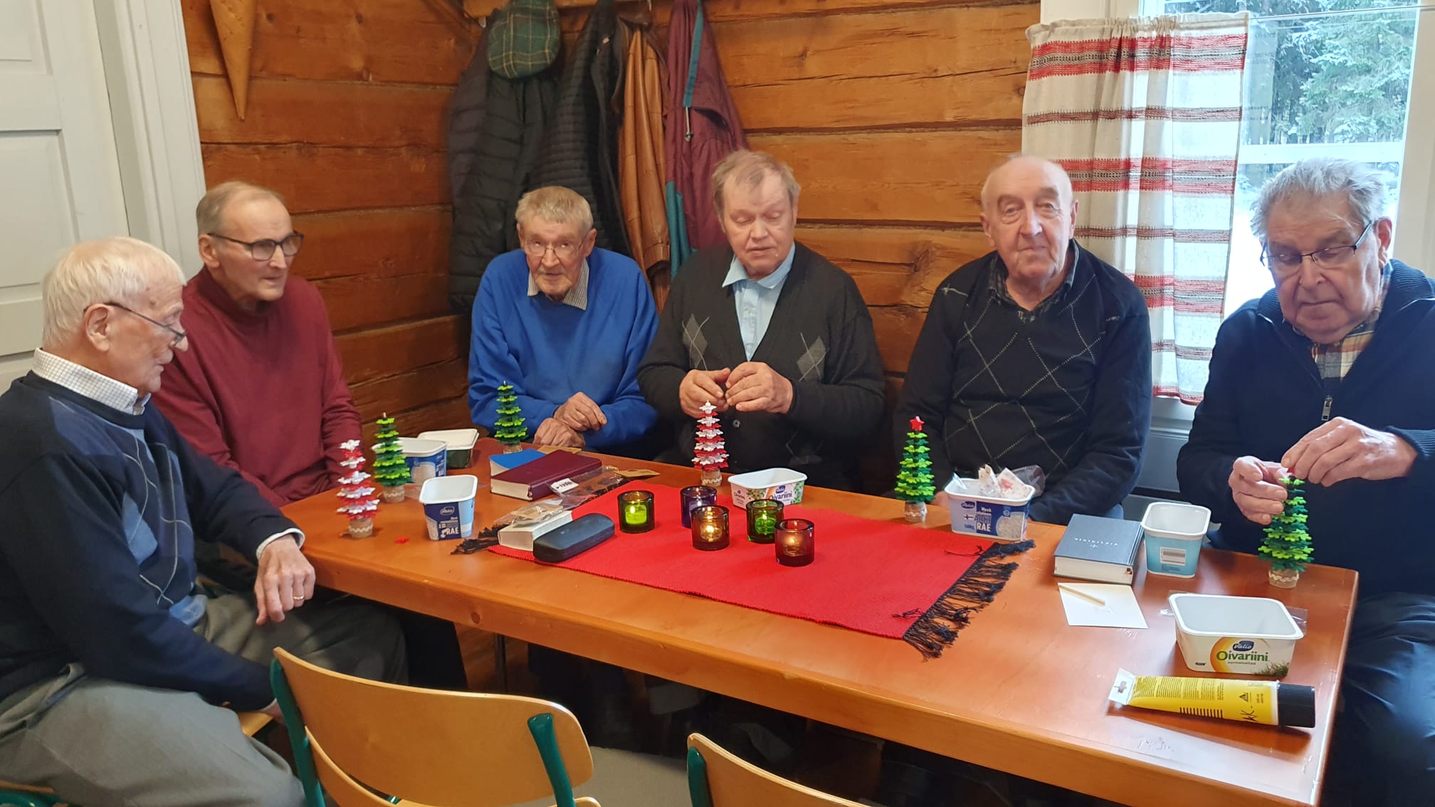 Miehet istuvat pöydän ympärillä ja askartelevat.